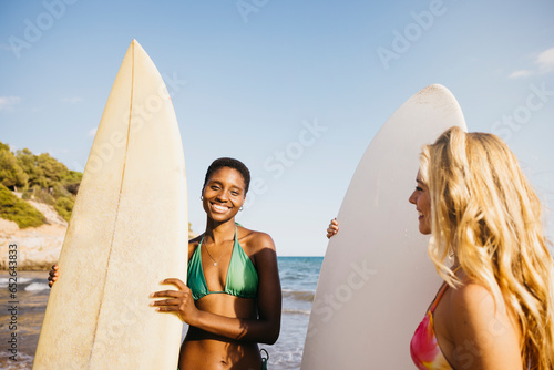 Portrait of two surfer friends on the beach in bikini, with her surfboard by her side. Women doing beach activities during summer vacation. © Jordi Salas