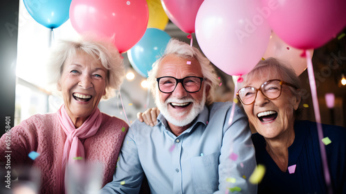 Portrait of happy group of senior people smiling and celebrating a birthday party with balloons and cake at a retirement home. Elderly people lifestyle