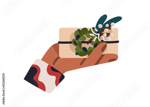 Holding gift box in holiday wrapping, decorated with fir wreath, leaf, plant....