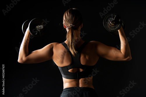 Strong woman with dumbbells. Slim girl holds dumbbells. Workout for sexy body. Fitness sexy woman with dumbbells on a dark background. Back view. Back of fitness woman. Slim woman with dumbbells.