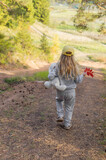 A little charming girl with long natural hair is walking in a beautiful forest in the autumn, she is holding a toy and red leaves in her hands