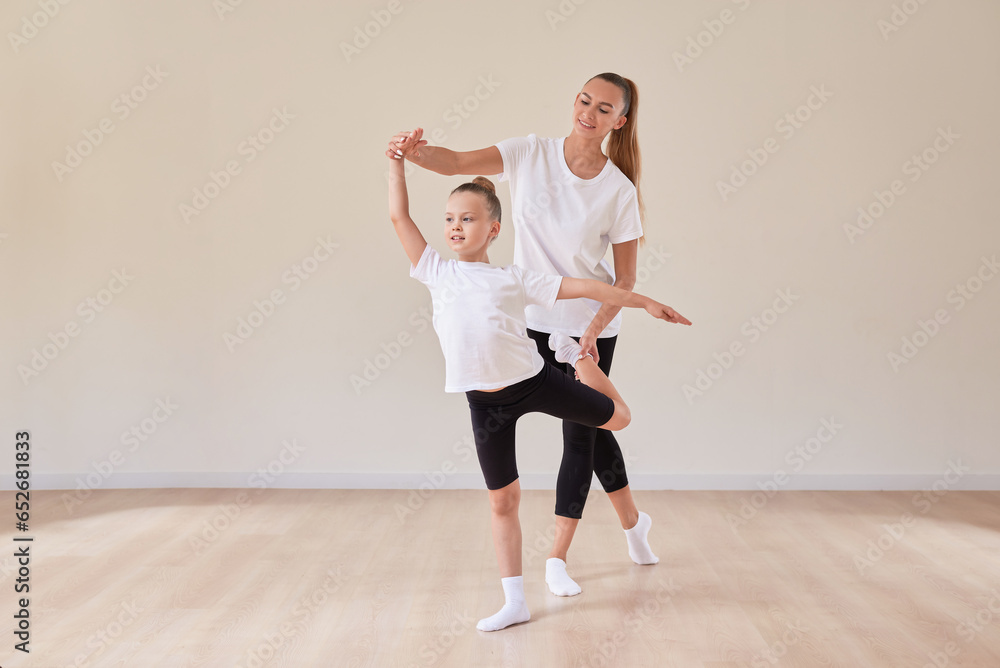 Fototapeta premium Beautiful woman teacher and a little girl perform dance movements in a bright studio. The concept of education, dance, sports, Pilates, stretching, healthy lifestyle.