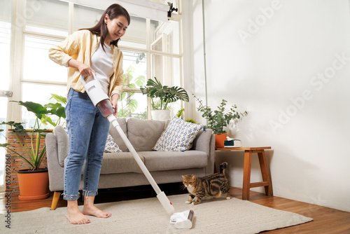 Young asian woman using vacuum cleaner machine to cleaning carpet and floor in living room at home in the weekend morning. Living lifestyle at home.