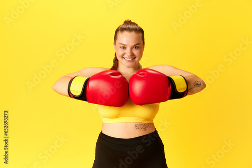 Image of young chubby sports woman in tracksuit and red in boxing gloves putting hands together isolated over yellow background