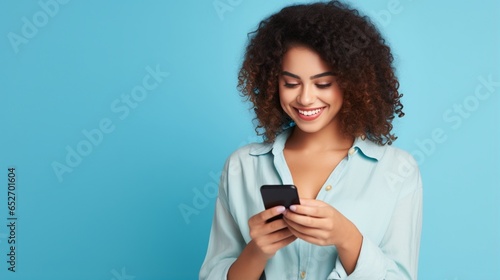 A young adult smiling happy pretty Latin woman holding a mobil phone typing messages and doing shopping on a cellphone isolated on a blue background. Generated with AI