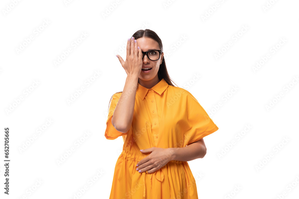 Caucasian young slender woman with black straight hair with glasses and in a yellow dress on a white background with copy space