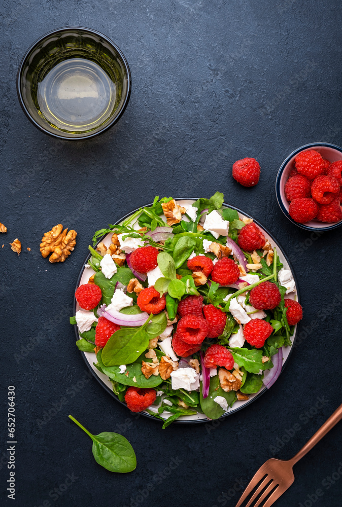 Gourmet salad with raspberries, white cheese, red onion, walnuts and mixed herbs, black table background, top view