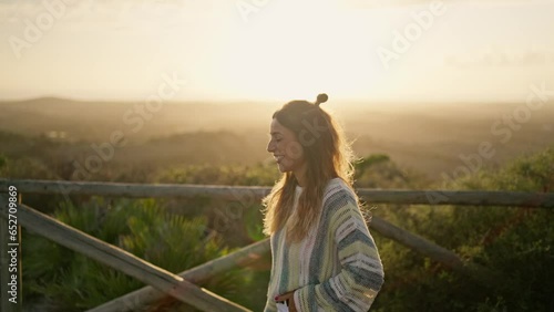 A smiling happy girl woman looks at camera in sunlight reflection outdoors. Beautiful teen cheerful girl smiling on hike nature. Closeup of a woman outside at sunrise sunset. Cinematic, slow motion photo