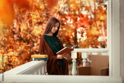Wallpaper Mural A girl reads a book on the balcony of her house. She is thoughtful, dressed in a green sweater and brown shawl. Season of the year is autumn. There are many autumn trees near the house. Torontodigital.ca