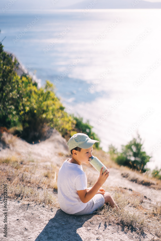 child on a cliff overlooking the sea drinks water, travel and active lifestyle