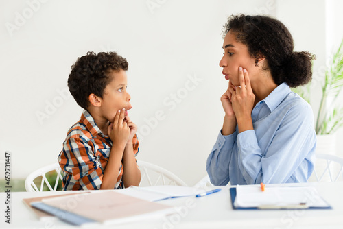 Woman working on boy pronunciation at speech therapy session indoors photo