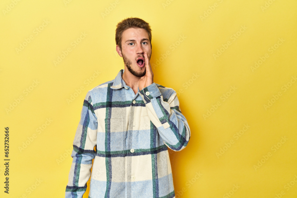 Young Caucasian man on a yellow studio background is saying a secret hot braking news and looking aside Young Caucasian man on a yellow studio background is saying a secret hot braking news and looking aside