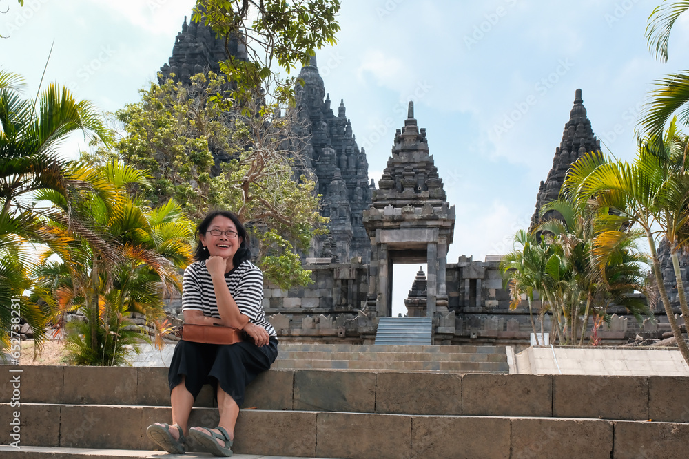 Asian female tourist sitting on a stone staircase at Prambanan temple, national park, Yogyakarta - Indonesia