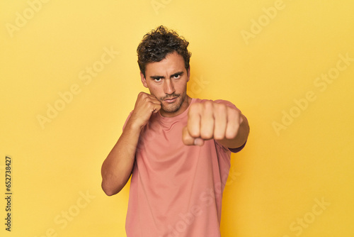 Young Latino man posing on yellow background throwing a punch, anger, fighting due to an argument, boxing.