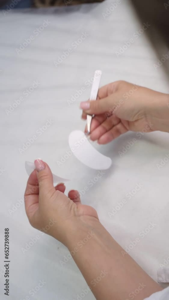 Video of hands of master removing sticker for white patch using tweezers and hanging thin consumable on finger. Female lashmaker preparing for applying material on lower eyelid of client. Vertical. Video of hands of master removing sticker for white patch using tweezers and hanging thin consumable on finger. Female lashmaker preparing for applying material on lower eyelid of client. Vertical.