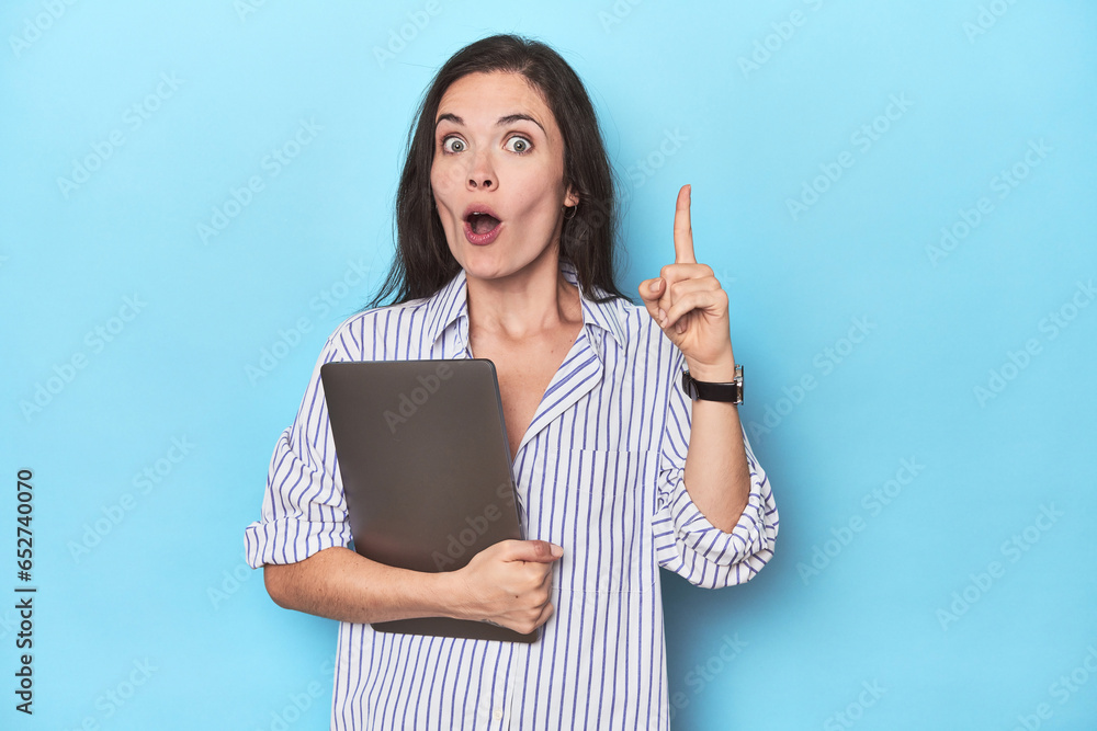 Young businesswoman holding laptop on blue having an idea, inspiration concept. Young businesswoman holding laptop on blue having an idea, inspiration concept.