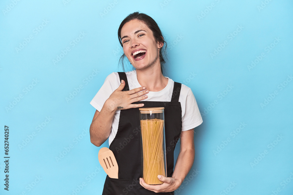 Chef woman with pasta jar on blue laughs out loudly keeping hand on chest. Chef woman with pasta jar on blue laughs out loudly keeping hand on chest.