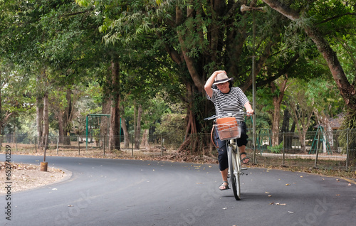 Woman riding bicycle and holding her hat under strong wind in the park