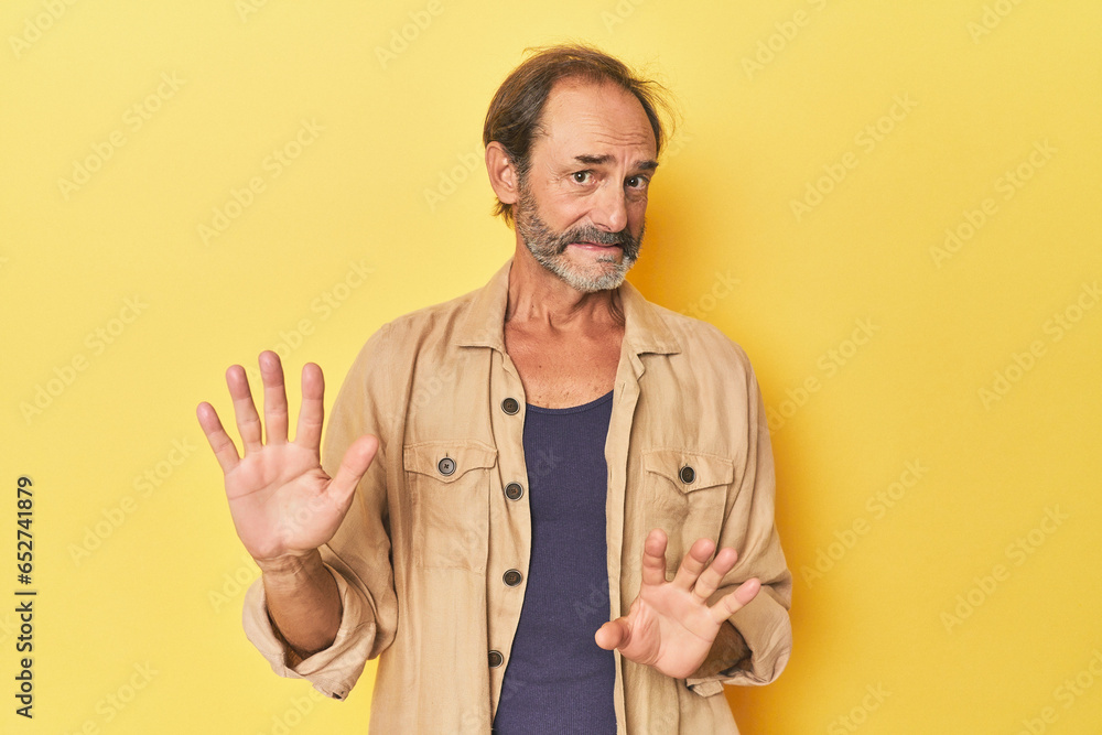Caucasian middle-aged man in yellow studio rejecting someone showing a gesture of disgust. Caucasian middle-aged man in yellow studio rejecting someone showing a gesture of disgust.