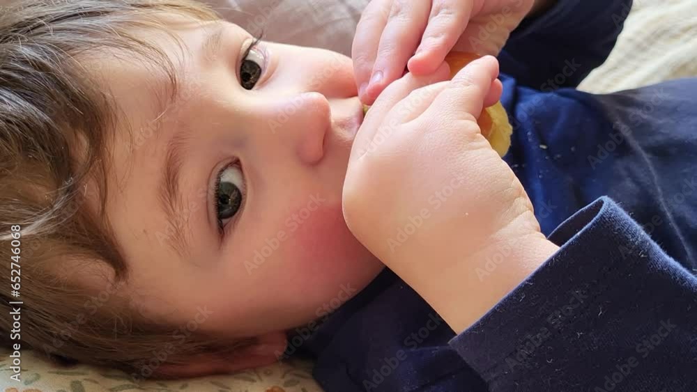 The toddler baby eat apple fruit lying on the couch