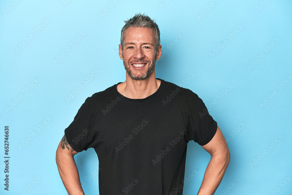 Obraz premium Middle-aged caucasian man on blue backdrop confident keeping hands on hips.