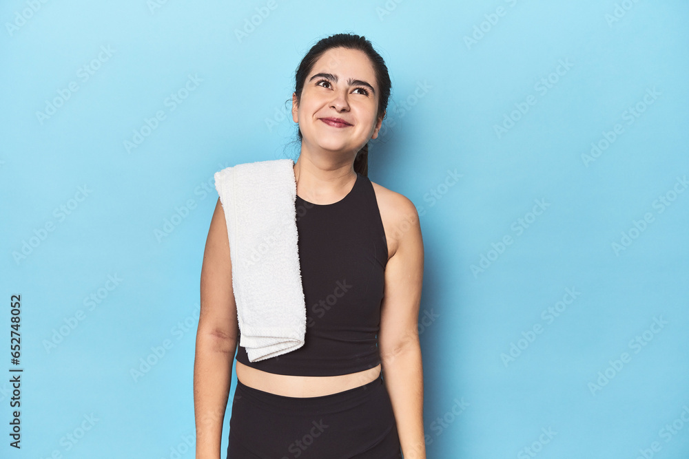 Sporty woman with towel on blue studio dreaming of achieving goals and purposes Sporty woman with towel on blue studio dreaming of achieving goals and purposes