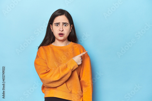 Young Caucasian woman on blue backdrop pointing to the side © Asier
