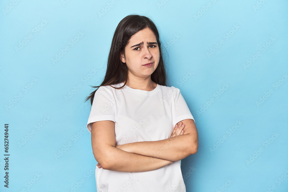 Young Caucasian woman on blue backdrop suspicious, uncertain, examining you. Young Caucasian woman on blue backdrop suspicious, uncertain, examining you.