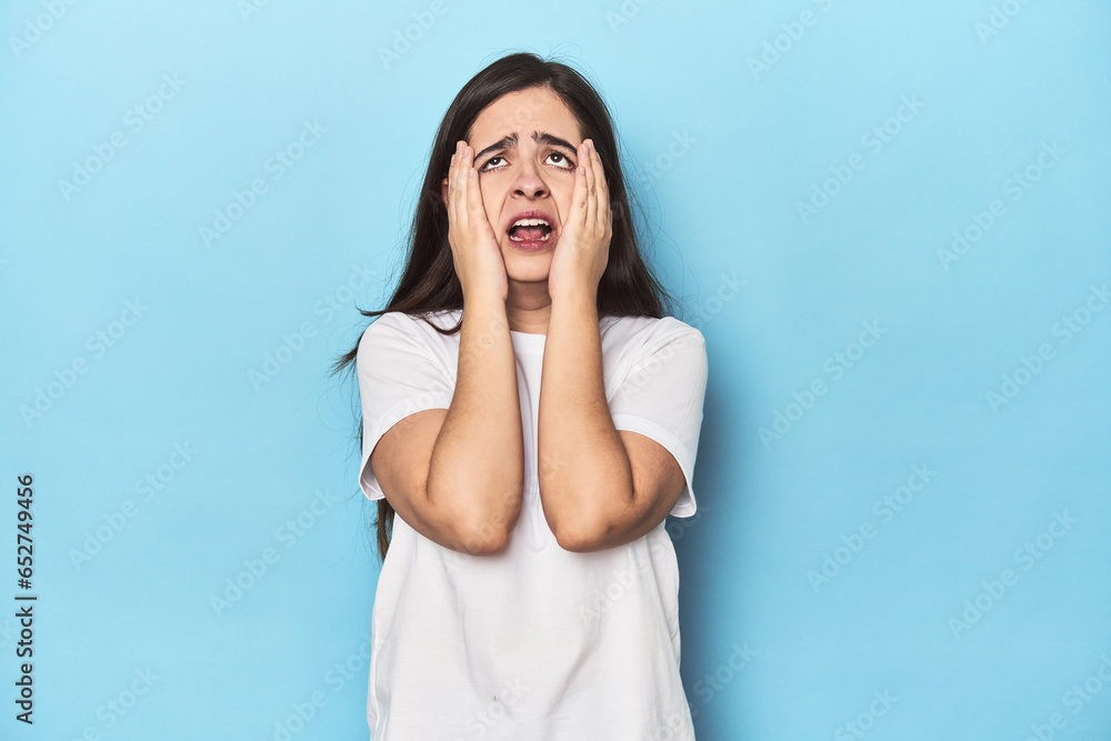 Young Caucasian woman on blue backdrop whining and crying disconsolately. Young Caucasian woman on blue backdrop whining and crying disconsolately.
