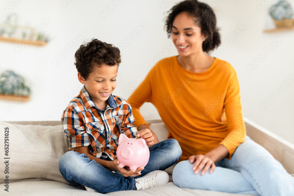 Fototapeta premium Happy Boy And Mom Holding Piggybank, Putting Coin At Home