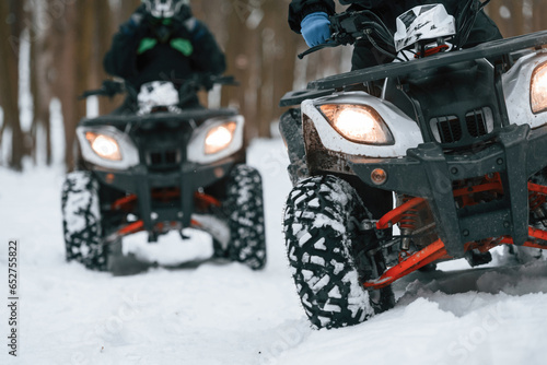 Two people are riding ATV in the winter forest