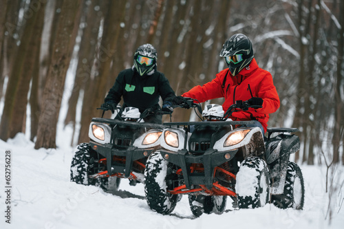 Conception of active recreation. Two people are riding ATV in the winter forest