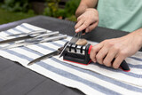 Close-up photo of man sharpening knives with special knife sharpener at home