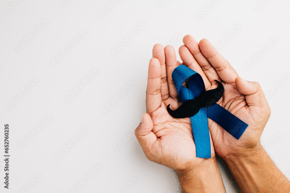 Fototapeta premium In November, men's health and Prostate cancer awareness take center stage. Man's hands embrace a light blue ribbon with a mustache on a blue background a symbol of support.
