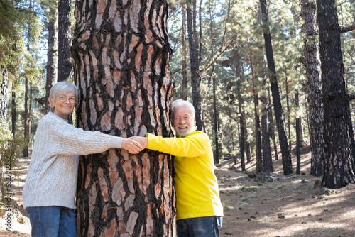 A lovely bonding happy senior couple embracing a big tree trunk enjoying a mountain hike in the forest expressing joy, freedom and love for nature © luciano