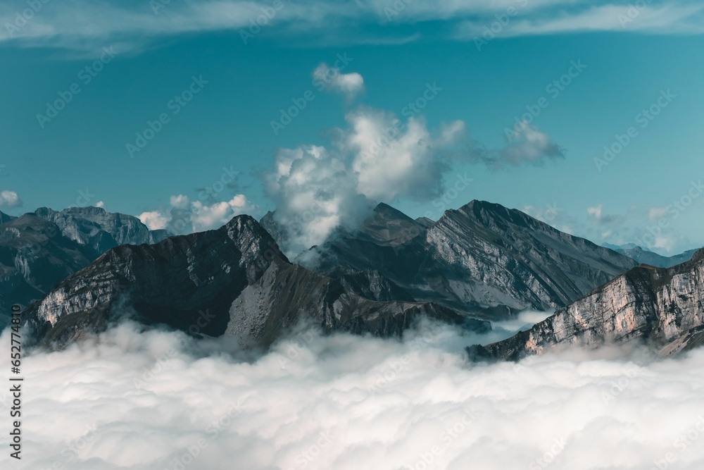 Obraz premium Scenic view of huge rocky mountains enveloped in white clouds in a blue sky background