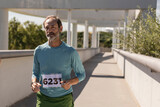 happy mature man running a marathon with bib number