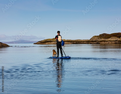 Man paddling in a lake with his dog on a calm day
