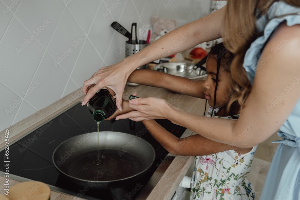 Mother is helping her daughter put oil in the pan.