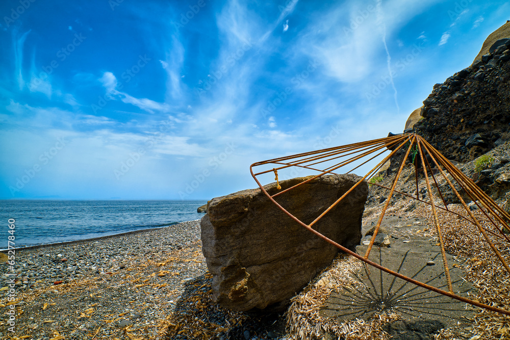 Rusty beach parasol carcass on grey volcanic beach on sunny day