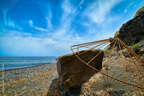 Obraz na płótnie Rusty beach parasol carcass on grey volcanic beach on sunny day w salonie