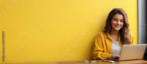 Smiling teen girl using laptop for online study on yellow background Happy student in educational webinar photo