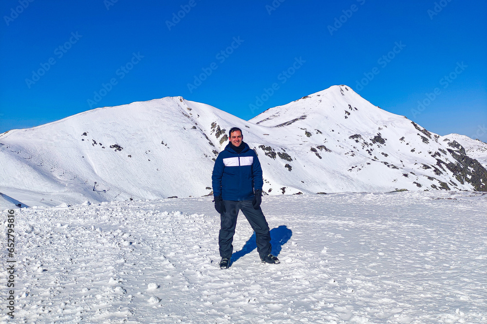A Young man posing in the Snow with a white background of the mountains of San Isidro ski station base in Spain