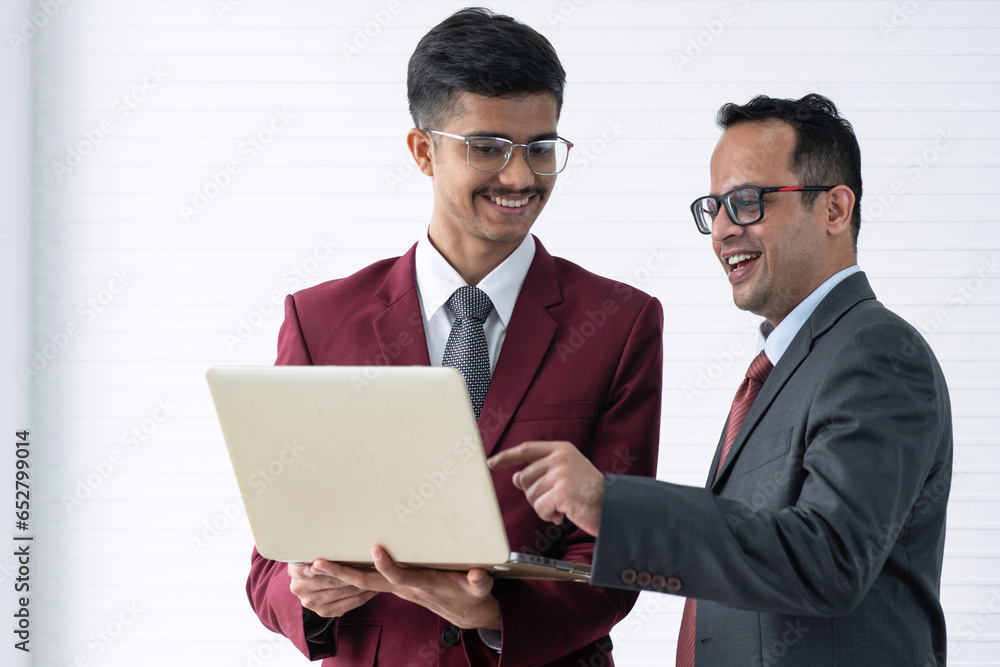 Young Indian businessman and senior manager watch and discuss new project on laptop screen together, cooperation concept Young Indian businessman and senior manager watch and discuss new project on laptop screen together, cooperation concept