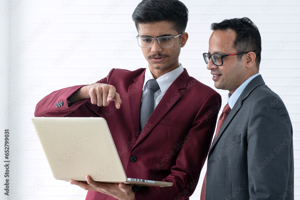 Young Indian businessman and senior manager watch and discuss new project on laptop screen together, cooperation concept Young Indian businessman and senior manager watch and discuss new project on laptop screen together, cooperation concept