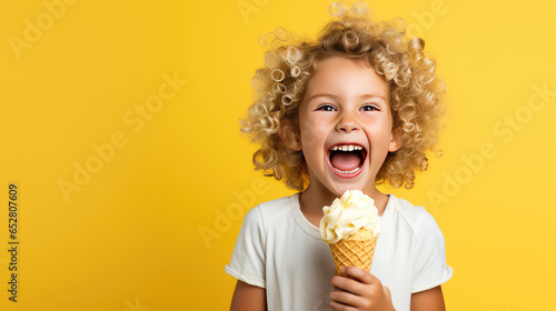 Cheerful happy child girl hold sweet ice cream in hands  eat ice-cream on flat yellow background with copy space. 