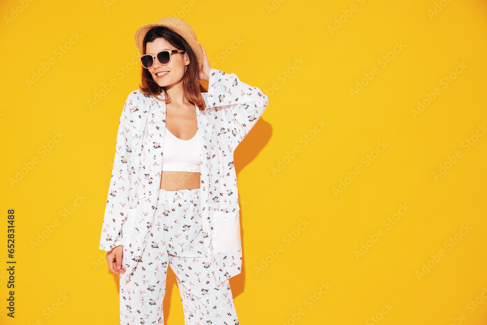 Young beautiful smiling female in trendy summer costume clothes. Carefree woman posing near yellow wall in studio. Positive model having fun indoors. Cheerful and happy. In hat and sunglasses Young beautiful smiling female in trendy summer costume clothes. Carefree woman posing near yellow wall in studio. Positive model having fun indoors. Cheerful and happy. In hat and sunglasses