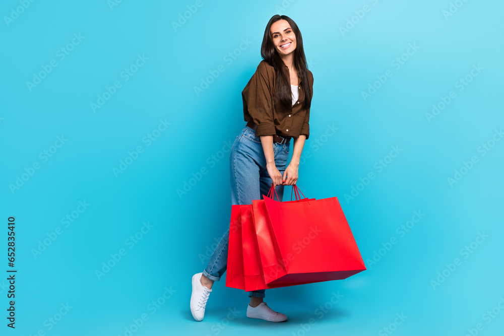 Full size body photo of dreamy good mood shopaholic hispanic young girl holding red bargains shiny isolated on blue color background