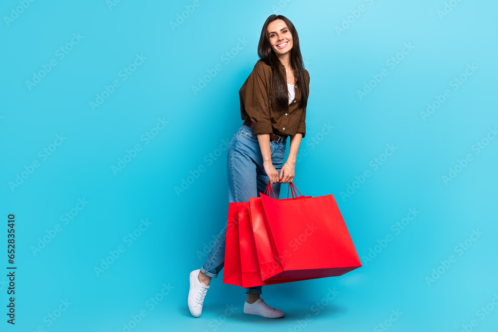 Full size body photo of dreamy good mood shopaholic hispanic young girl holding red bargains shiny isolated on blue color background Full size body photo of dreamy good mood shopaholic hispanic young girl holding red bargains shiny isolated on blue color background