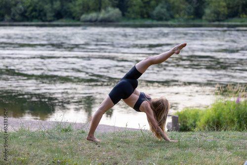 Beautiful young woman doing yoga exercise in nature by the river